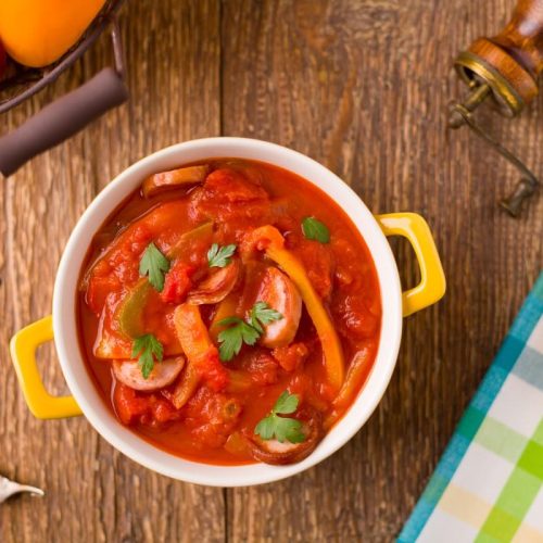 Letcho Polonais : ragoût à la saucisse et aux poivrons, servi dans un bol avec des anses jaunes, sur une table rustique en bois, vue du dessus