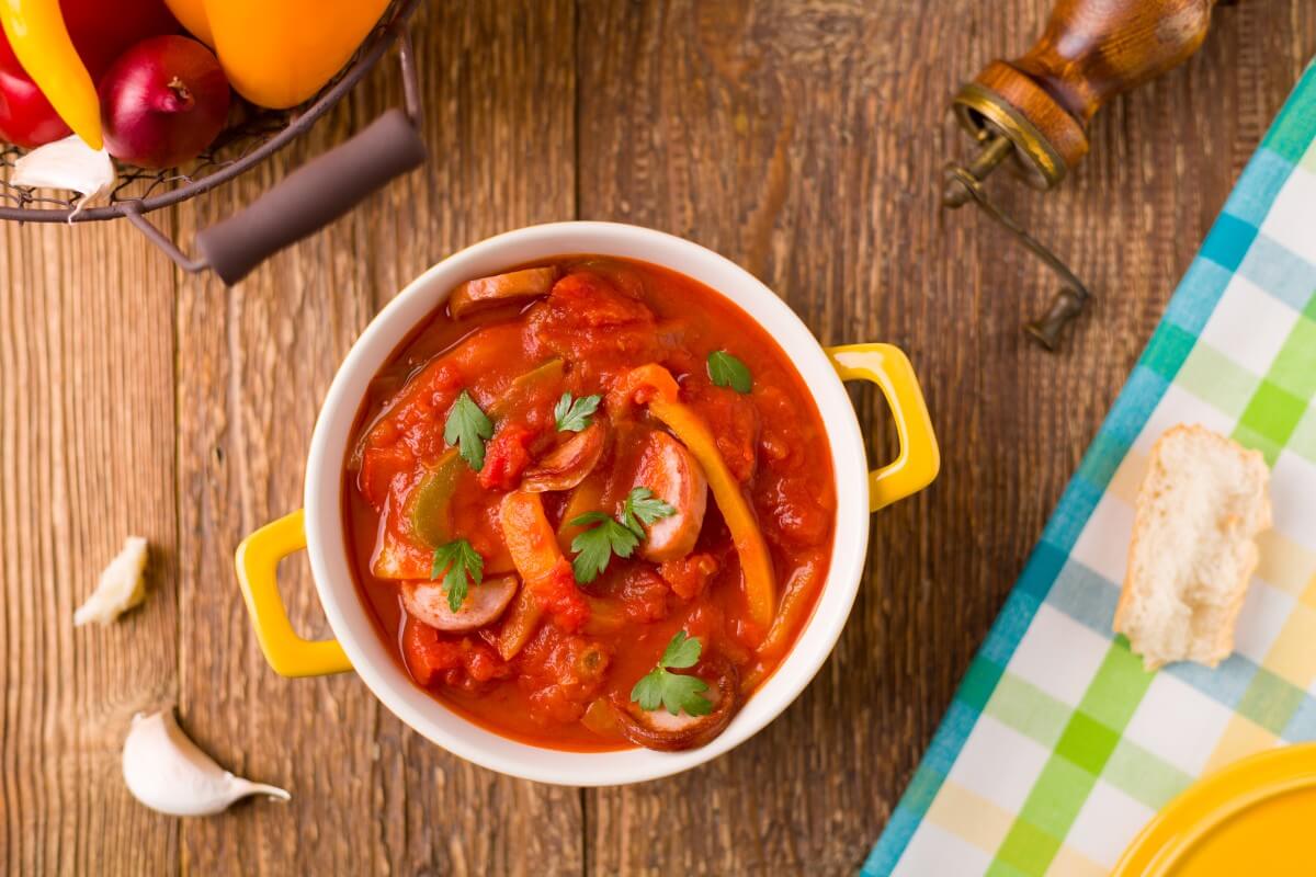 Letcho Polonais : ragoût à la saucisse et aux poivrons, servi dans un bol avec des anses jaunes, sur une table rustique en bois, vue du dessus