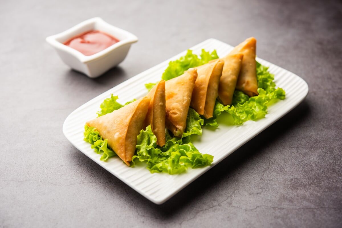 Samoussa au kiri et au poulet présentés sur une assiette blanche rectangulaire sur un lit de salade et avec un petit pot de ketchup