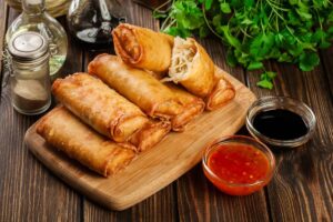 Nems au porc et aux crevettes présentés sur une planche en bois avec de la salade et des sauces