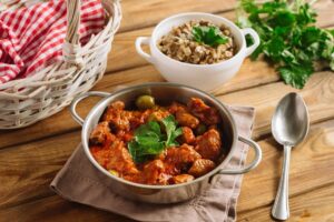 Râgout de veau aux olives vertes, présenté dans un plat en métal sur une table en bois