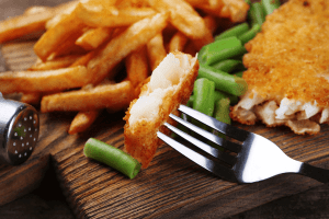 Poisson pané de merlan servi avec des frites, un morceau mis en avant piqué sur une fourchette