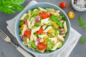 Salade de penne à l'italienne avec des tomates cerises, du concombre, de la roquette et des oignons rouges, servie dans un saladier moderne