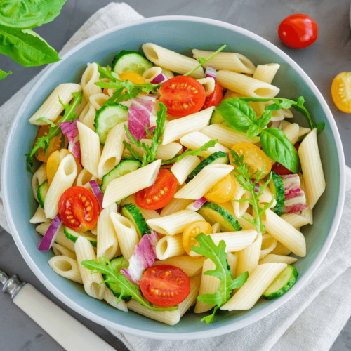 Salade de penne à l'italienne avec des tomates cerises, du concombre, de la roquette et des oignons rouges, servie dans un saladier moderne