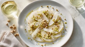 Carpaccio de poire au parmesan avec des éclats de pistaches et de noix servi dans une assiette élégante digne d'un restaurant gastronomique.