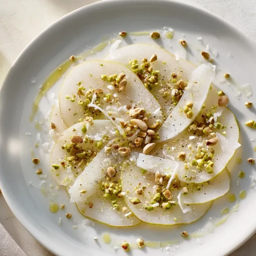 Carpaccio de poire au parmesan avec des éclats de pistaches et de noix servi dans une assiette élégante digne d'un restaurant gastronomique.