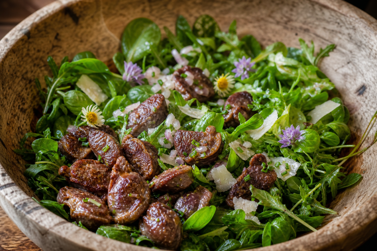 Salade verte avec gésiers de canard dorés, croûtons à l'ail et vinaigrette dans un saladier en bois