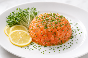 Tartare de saumon frais à la ciboulette, présenté en dôme sur une assiette blanche avec des tranches de citron