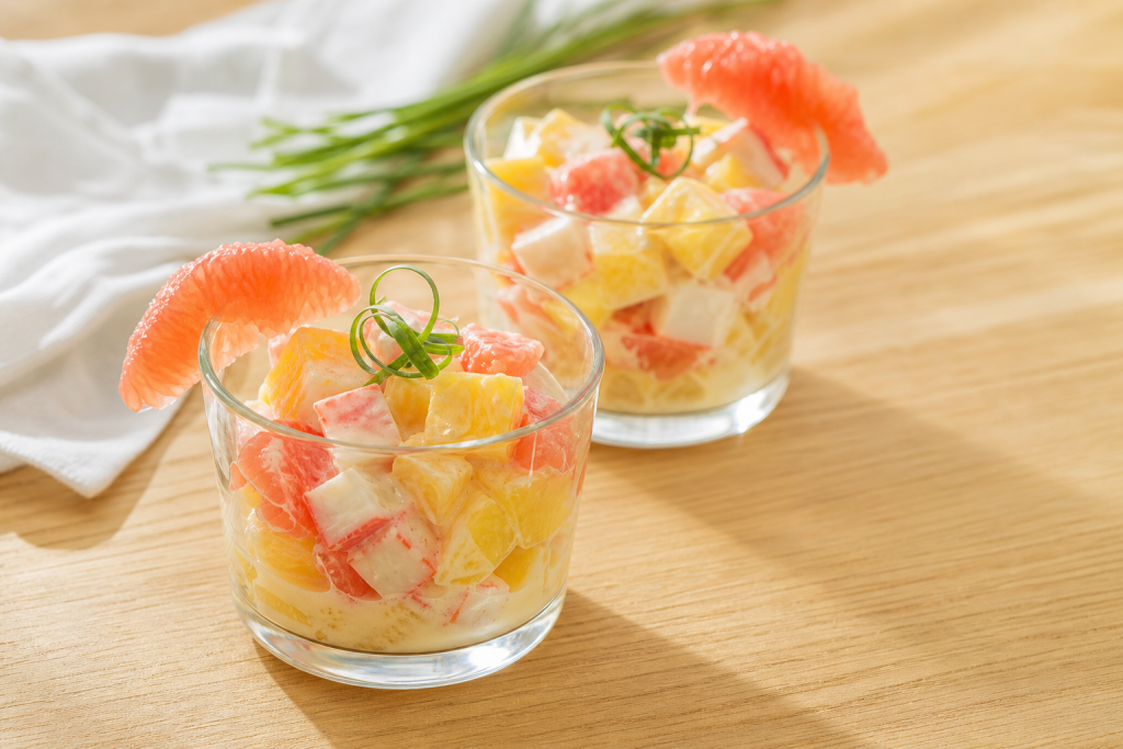 Verrines transparentes avec dés d'ananas, suprêmes de pamplemousse rose et surimi, décorées de ciboulette