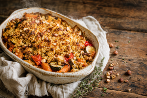 Crumble de légumes à la noisette dans un plat en céramique, avec une croûte dorée et des légumes colorés visibles.