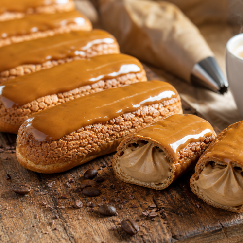 Éclairs au café dorés avec glaçage brillant, disposés sur une planche en bois, l'un coupé montrant la crème pâtissière au