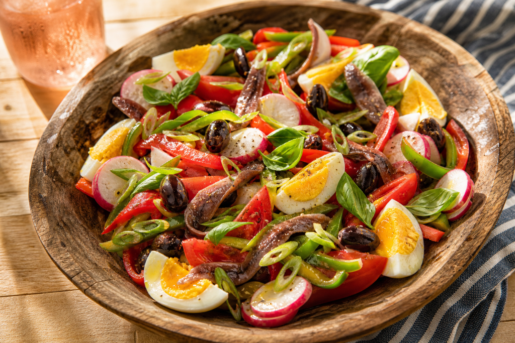 Salade niçoise traditionnelle avec tomates, œufs durs, anchois, olives noires, poivrons et basilic frais